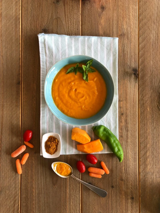 small bowl of carrot soup on wooden table with napkin and spoons