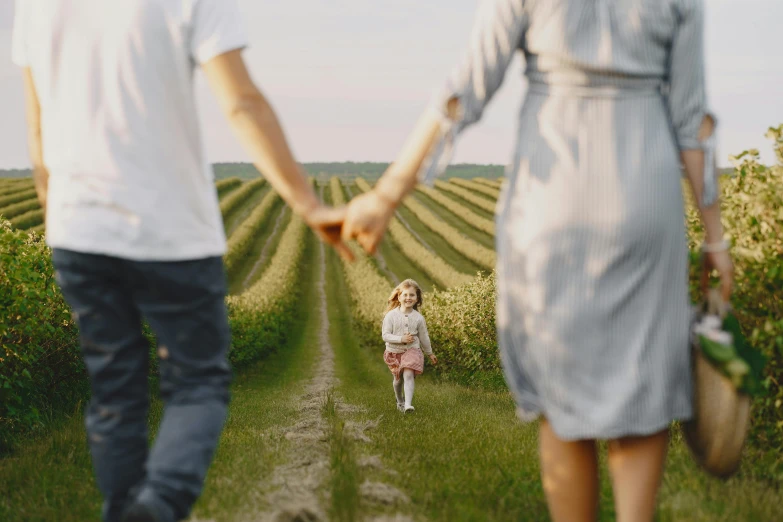 a woman holding the hand of a child who is walking through an open field