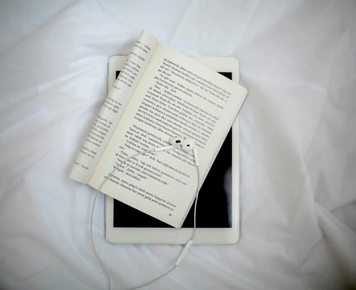 two electronic devices and an old book lying on a sheet