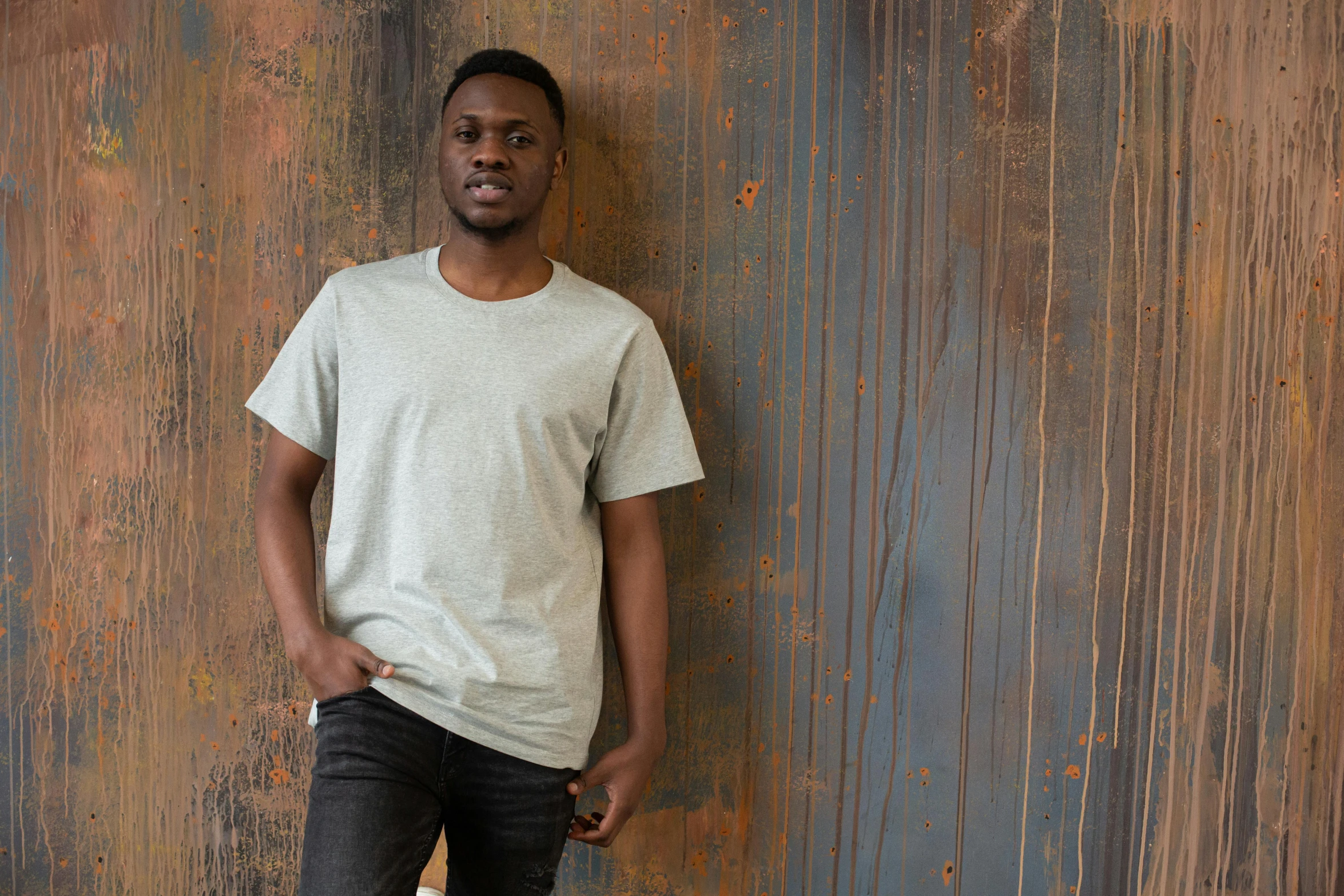 a black man in a white shirt leaning against a wood wall