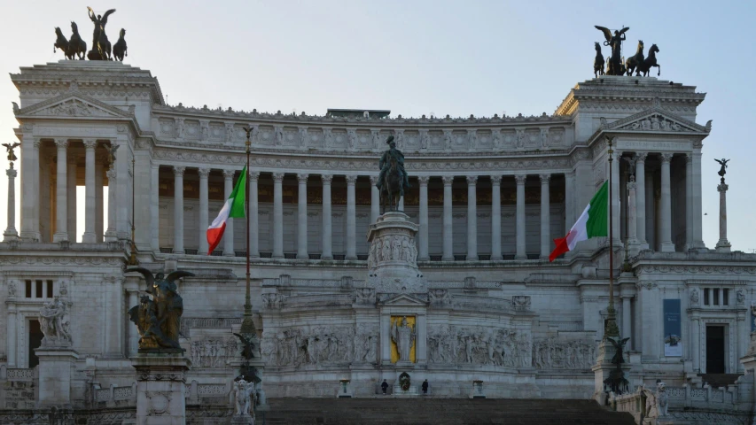 a building that has statues in it and two flags flying