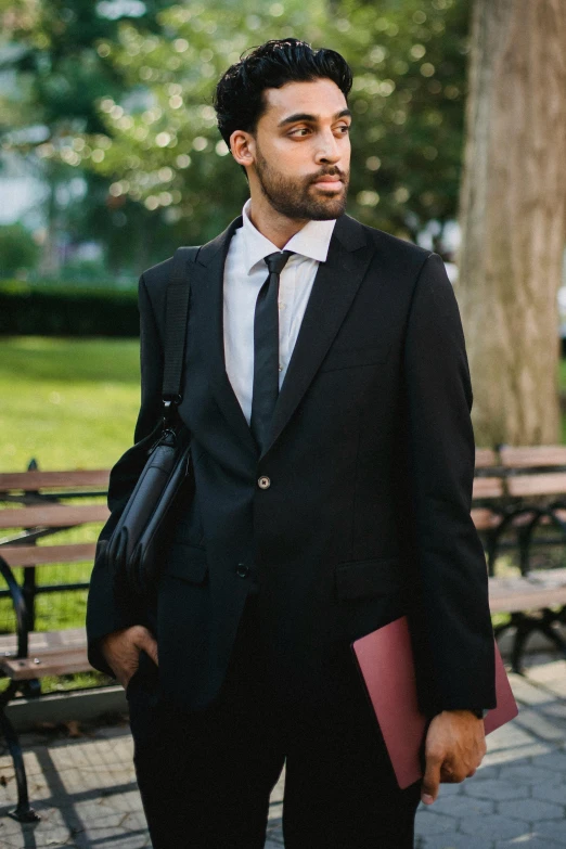 the young man in a suit and tie is holding a notebook and a bag