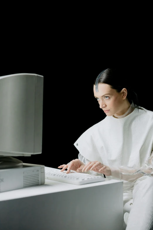 woman in white sitting at computer with black background