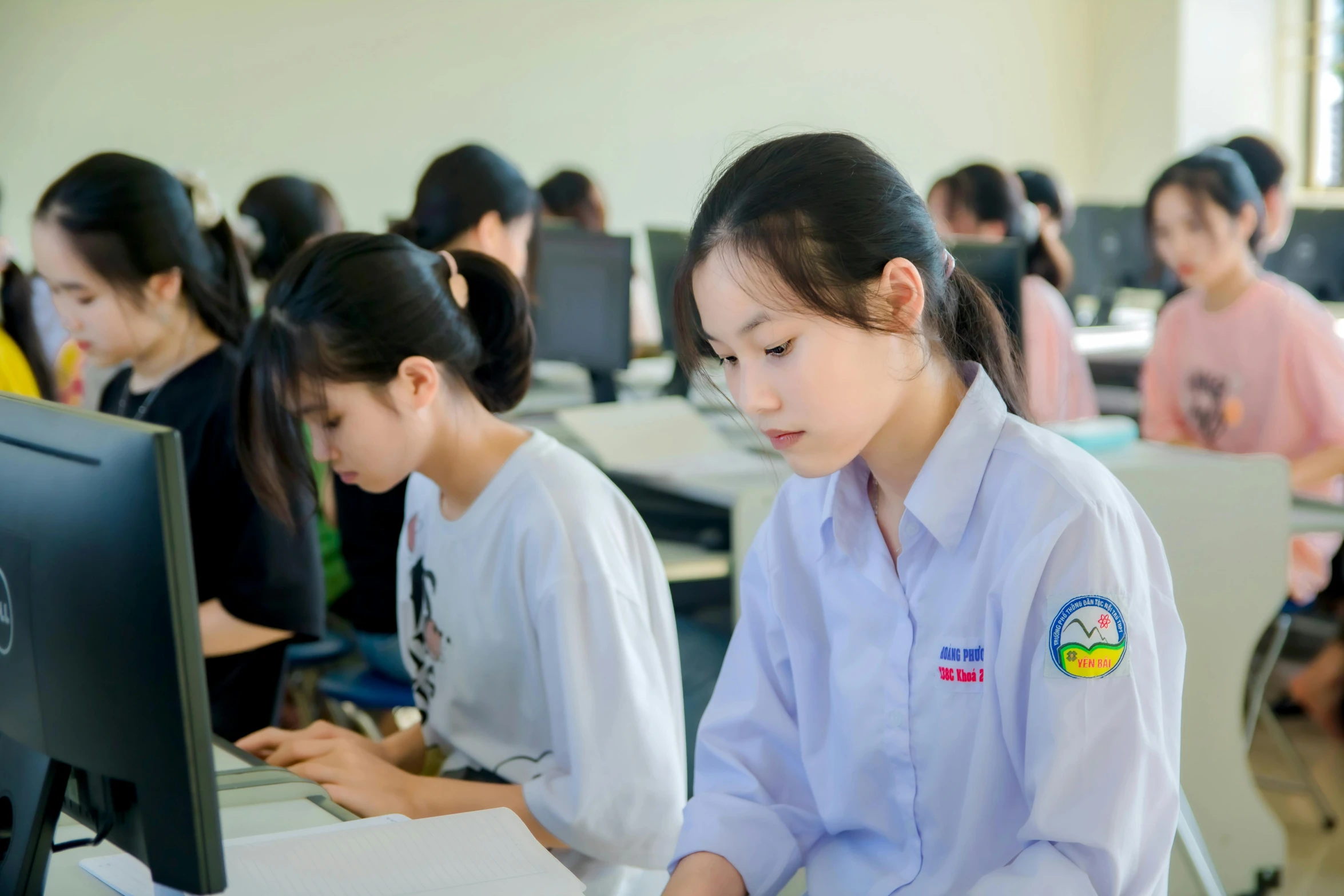 there are children at desks in an school with one sitting at the computer