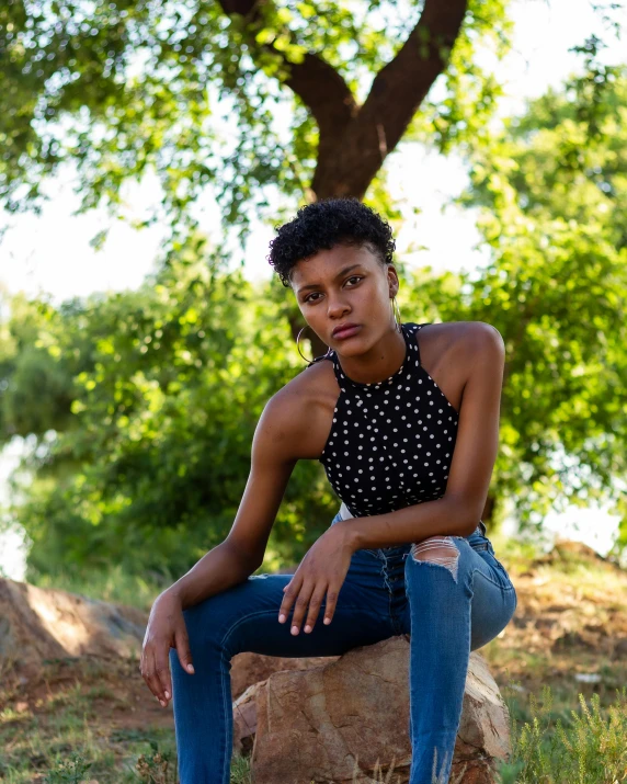 a girl in a polka dot top and jeans sitting on a rock