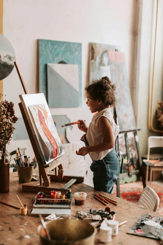 a girl holding a brush painting on an easel