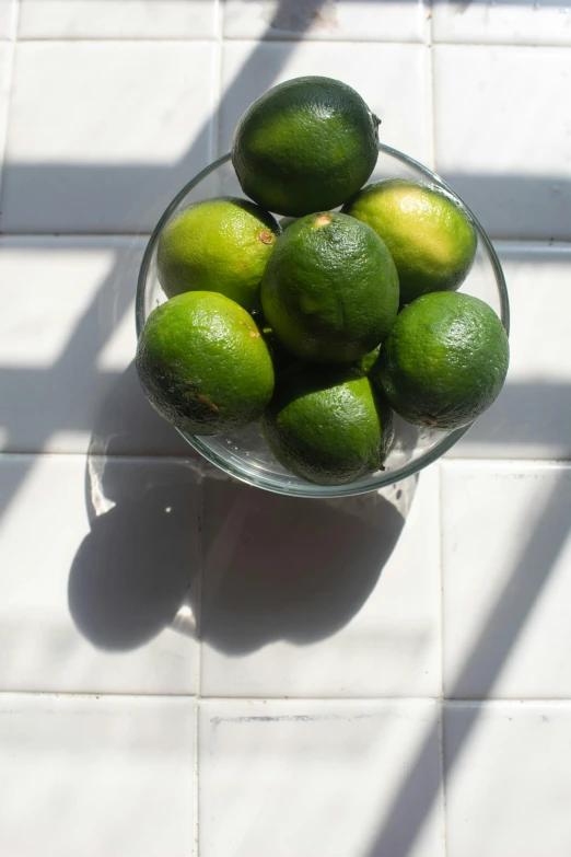 a glass bowl with limes on a tile floor