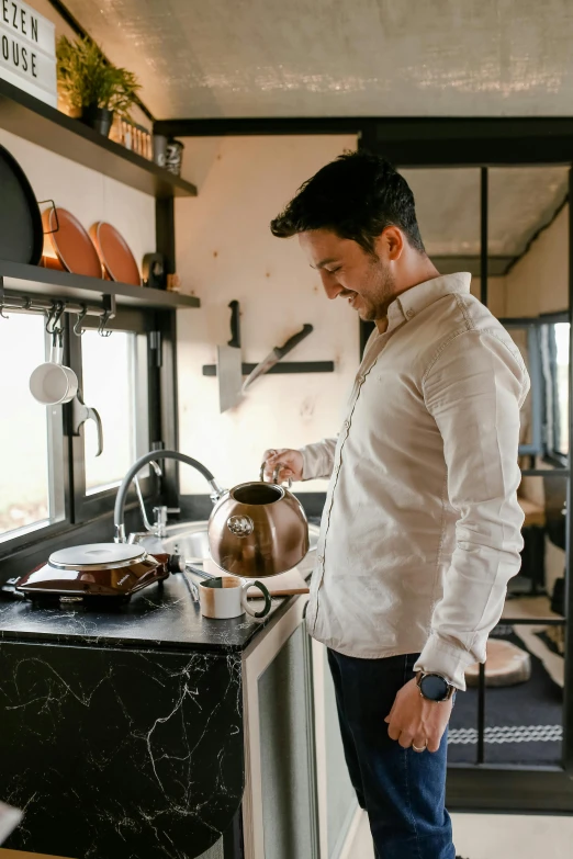 a man in white jacket holding a tea kettle in his hand and standing in kitchen