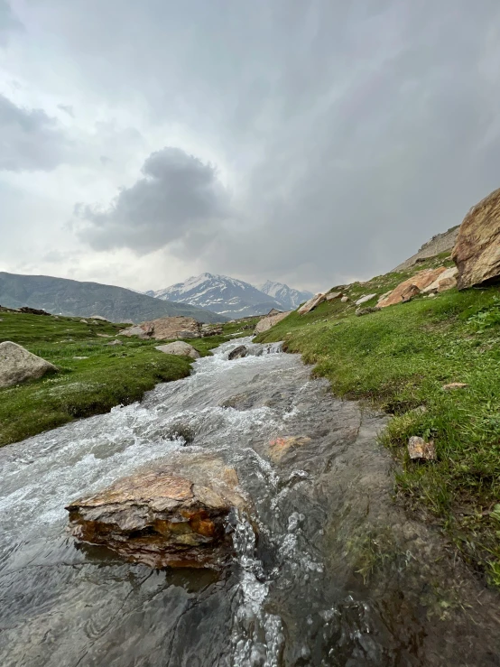 small creek running between two mountains in a grassy field