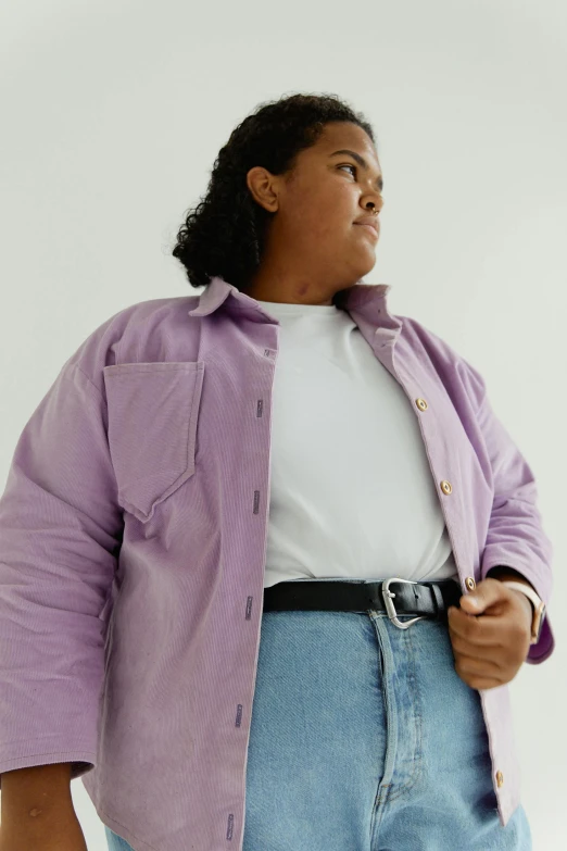 a woman in a purple shirt and jean pants stands against a white background