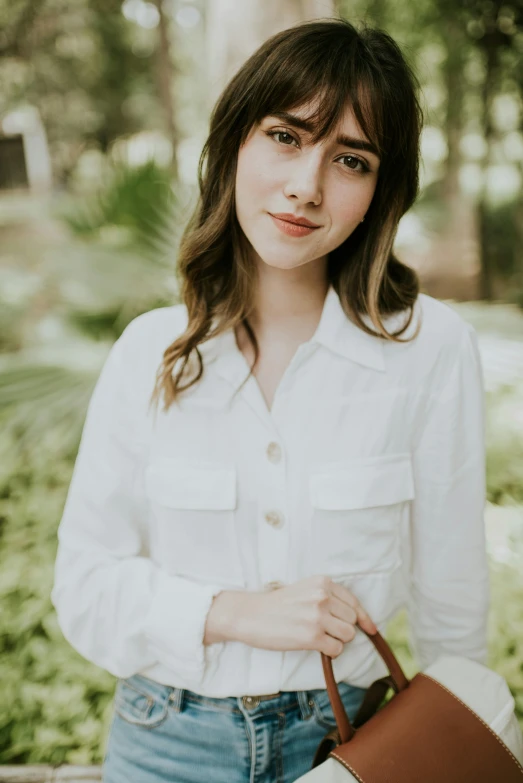 a woman in a white shirt and jeans holding a brown bag