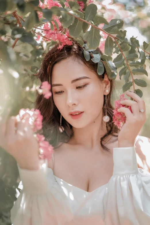 woman with white top smelling flowers on a bush