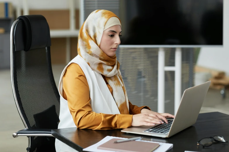 a woman is sitting at a desk working on her laptop