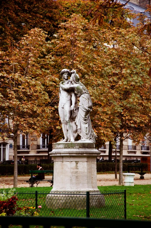 the statue sits next to a park bench on green grass