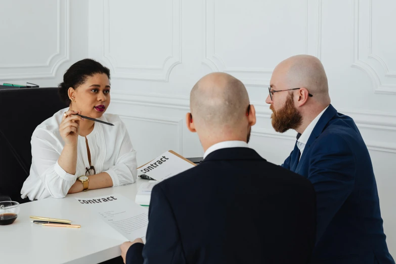 a woman with a pen sits talking to three men in an office