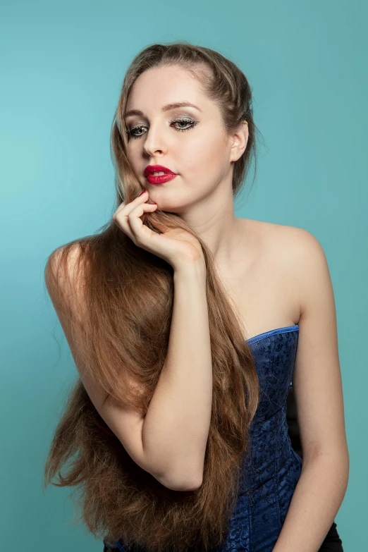 a woman in a strapless blue dress holding her long hair back to the camera with her hand