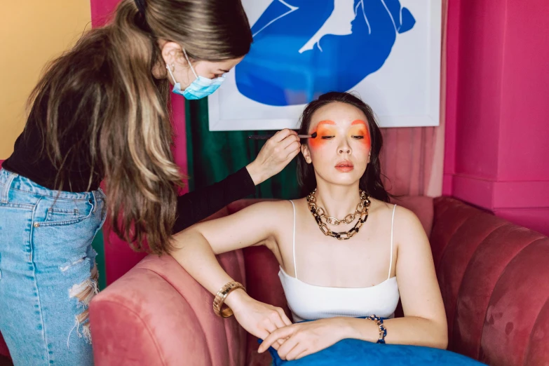 a woman getting her face painted sitting next to another lady