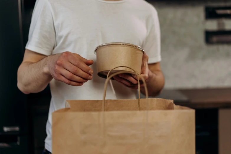 a man holds a brown paper bag and a brown cup in his hands