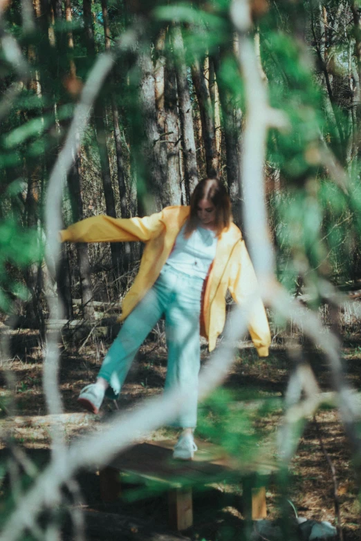 a girl is standing on a log and throwing a yellow jacket