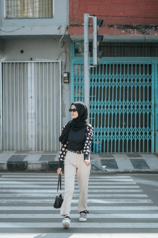 a woman crosses the street while wearing a hijab and holding a cross walk