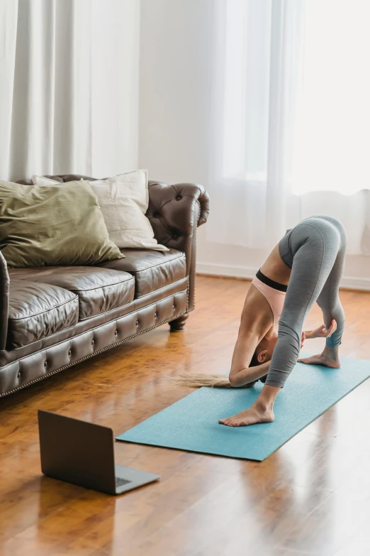 a woman doing yoga with a laptop and a couch in the background