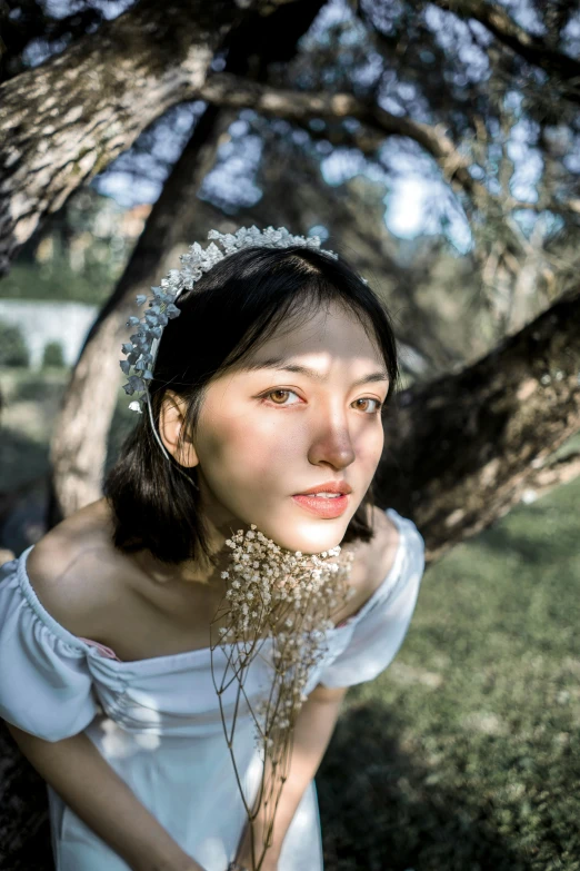 a young woman standing under a tree in a white dress