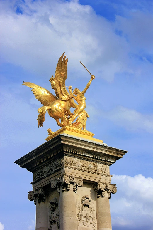 gold statue with angel atop on top against blue sky