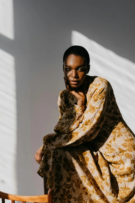 an african american woman sitting on a chair wearing a brown and tan dress