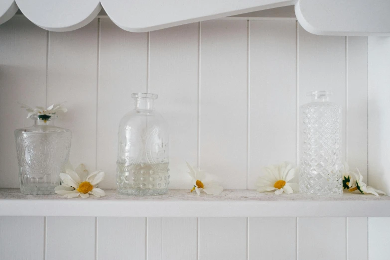 three glass vases and one white flower sitting on a shelf