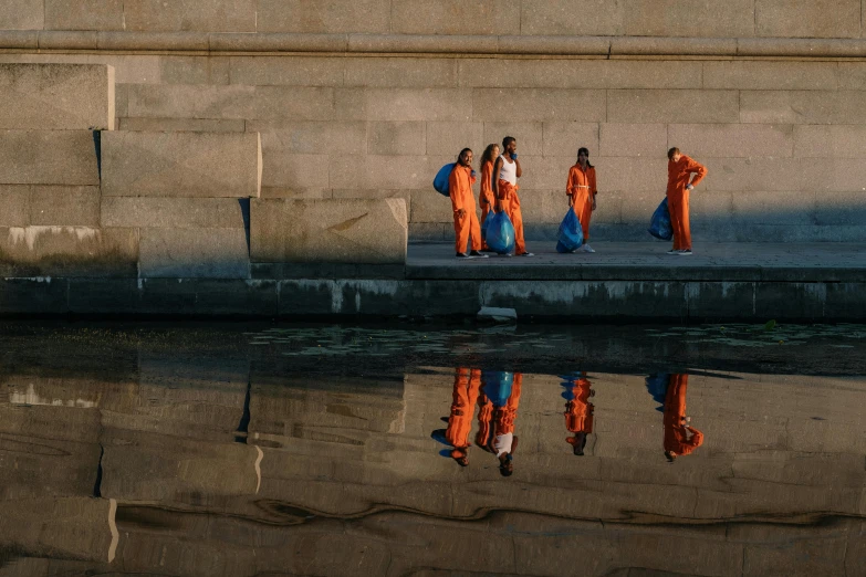 a group of three women in orange bathrobes next to a body of water