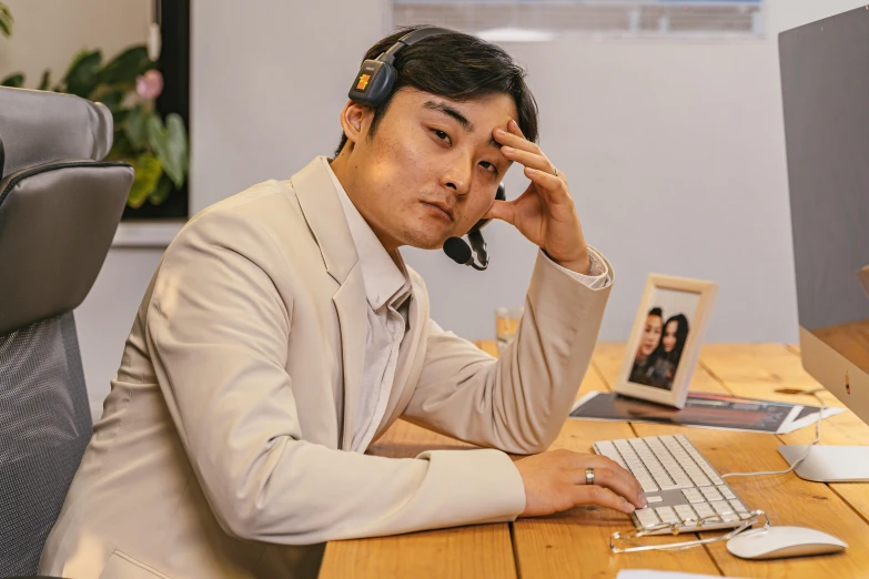 an asian man working on his computer while holding a headset