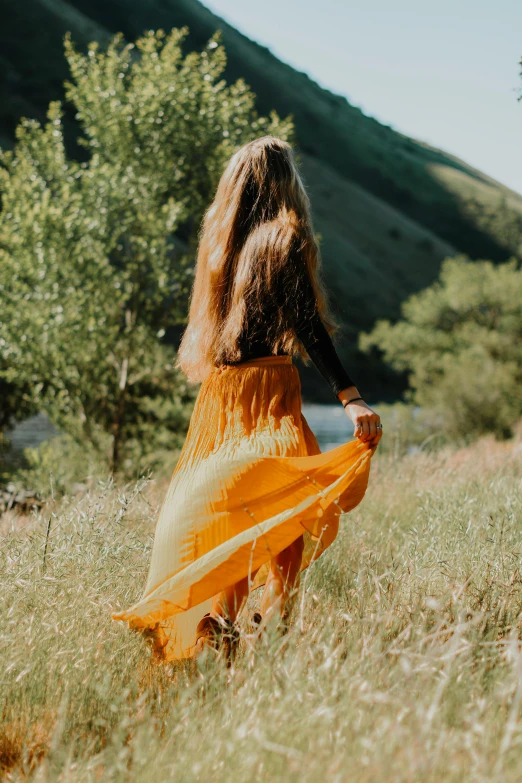 the back view of a woman in yellow dress walking through a grassy field