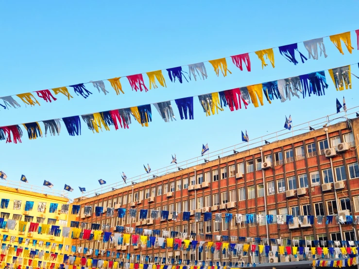 many colorful flags flying in the wind and a building with other buildings in the background