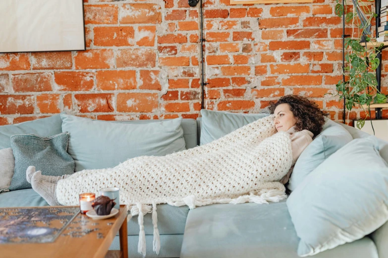 a woman is sleeping on a couch in front of a brick wall