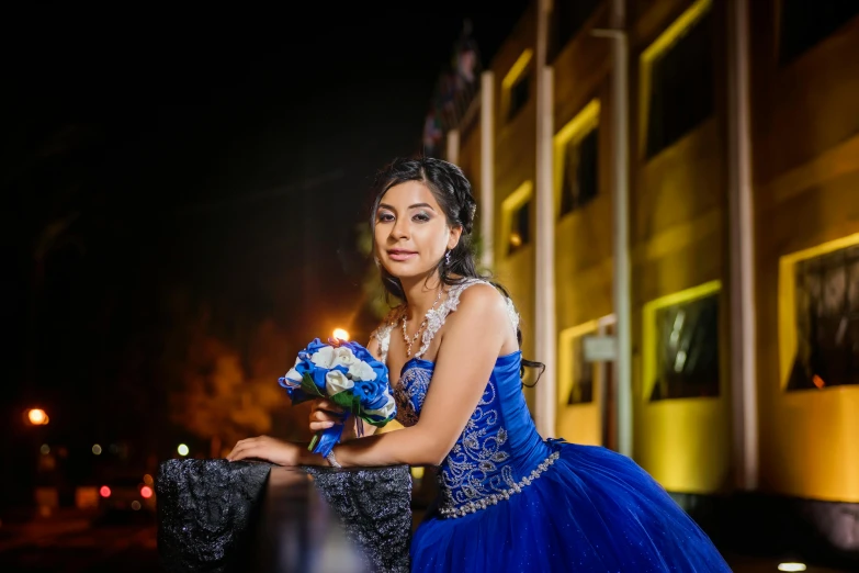 a bride wearing a blue gown holding a bouquet poses on a street