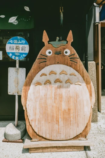 a wooden art piece of totoro sitting outside a shop