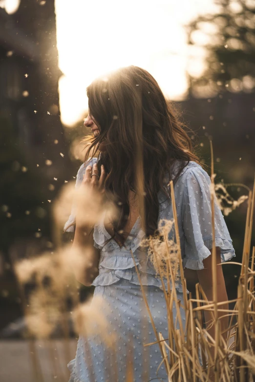 a woman is standing in tall grass with the sun shining behind her