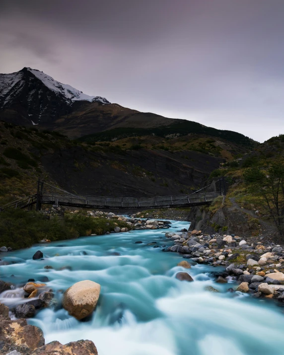 a small river running alongside a mountain and bridge