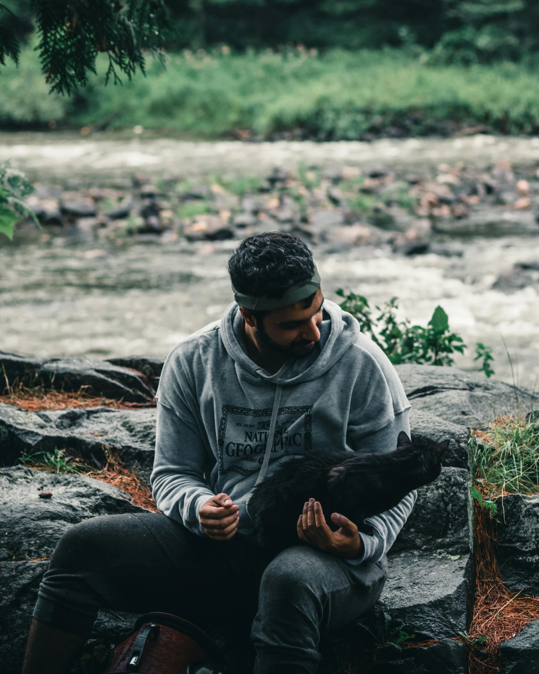 a man and a cat sitting on rocks near a river