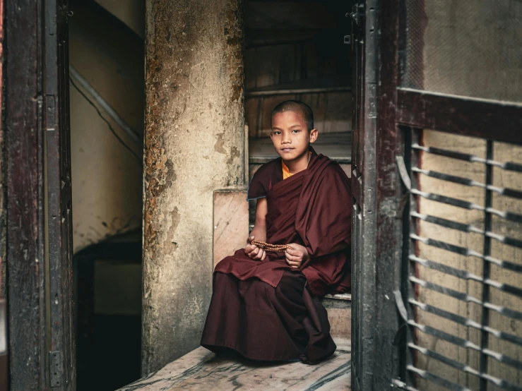 a young monk sits outside of his home