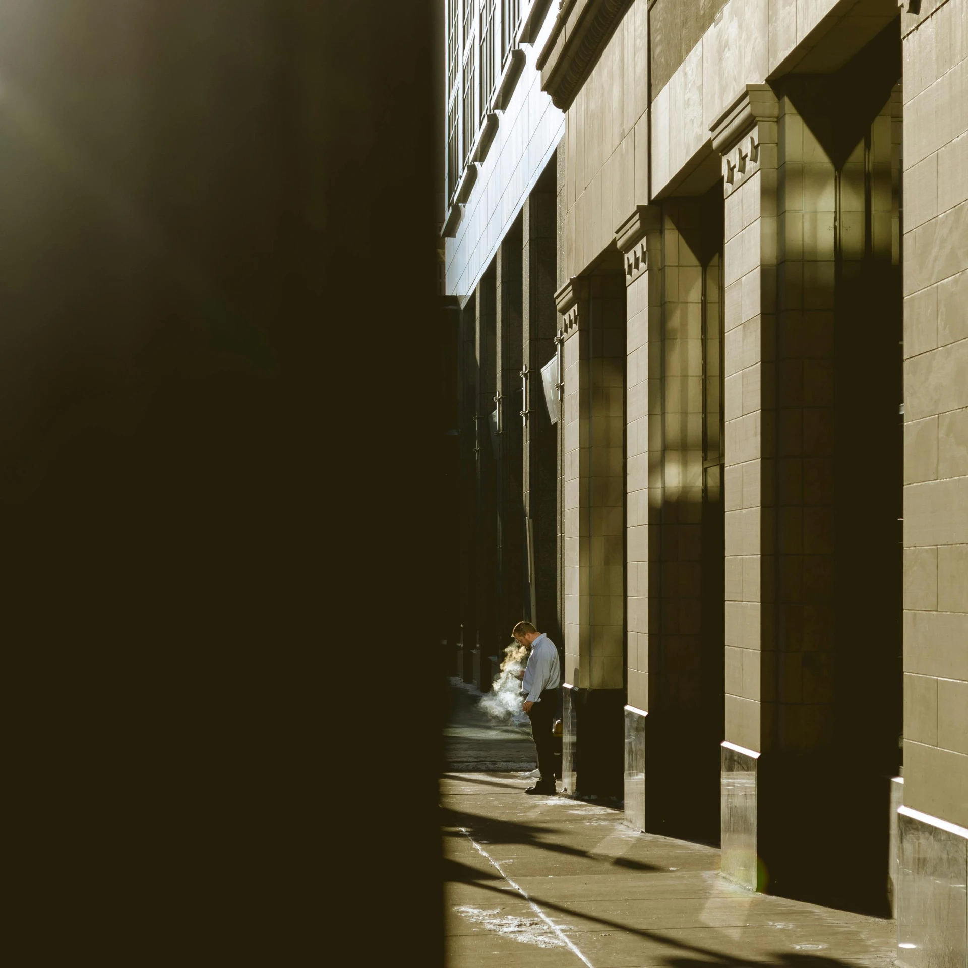 two people standing next to a wall while a man on his cell phone walks down the street