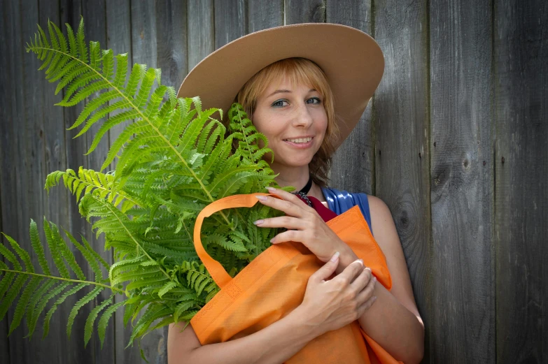 woman in orange scarf holding large fern and a hat