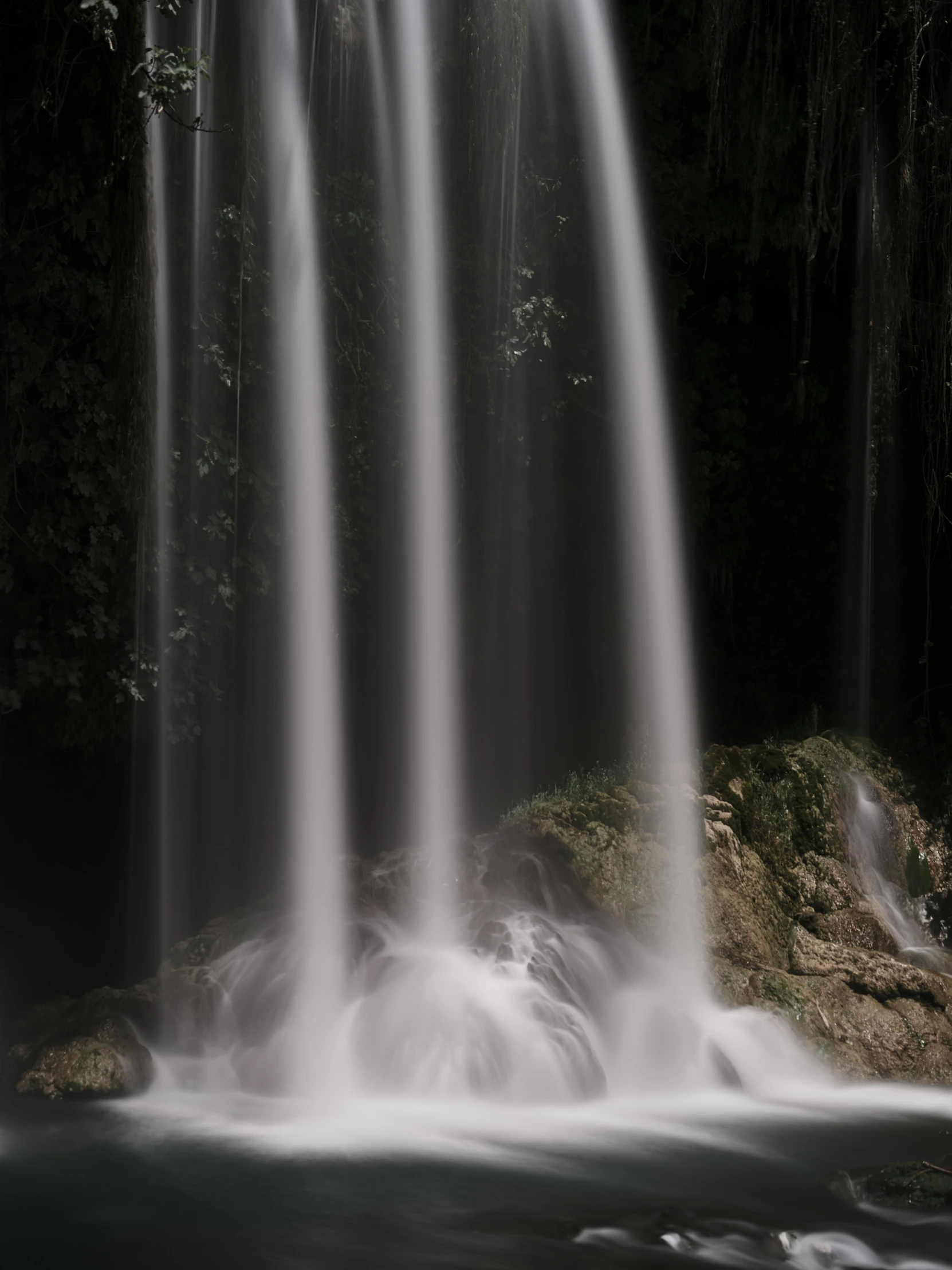 a waterfall falling into water in front of some green vegetation