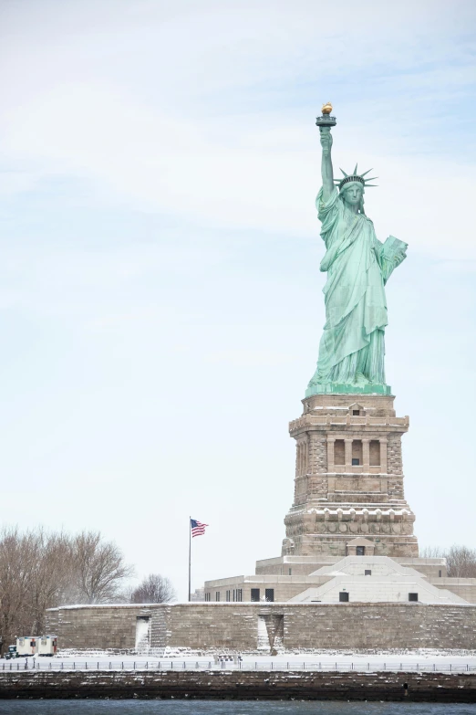 statue of liberty sits in the middle of a body of water with a large american flag flying next to it