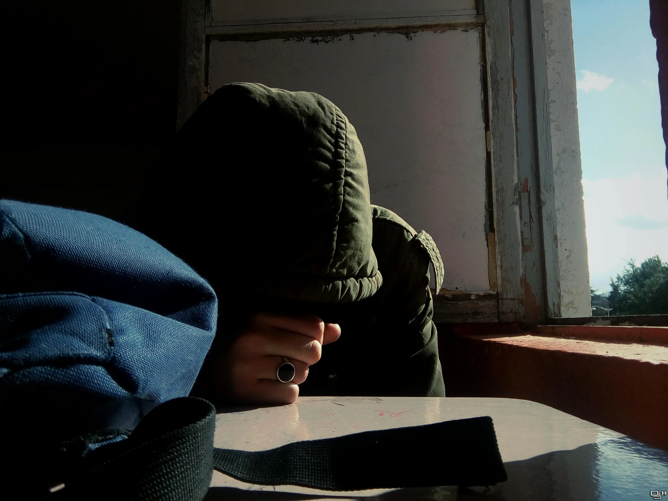 a person in a hooded jacket, looking at soing outside of a window