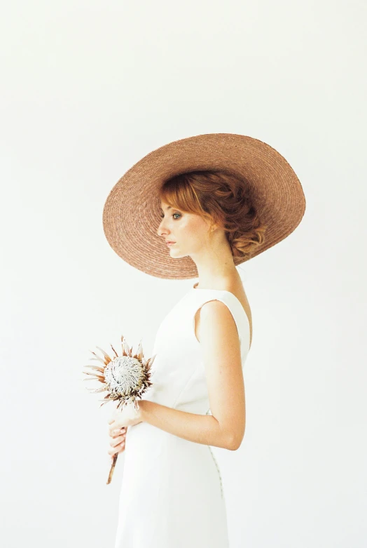 woman in white dress and straw hat against a light background