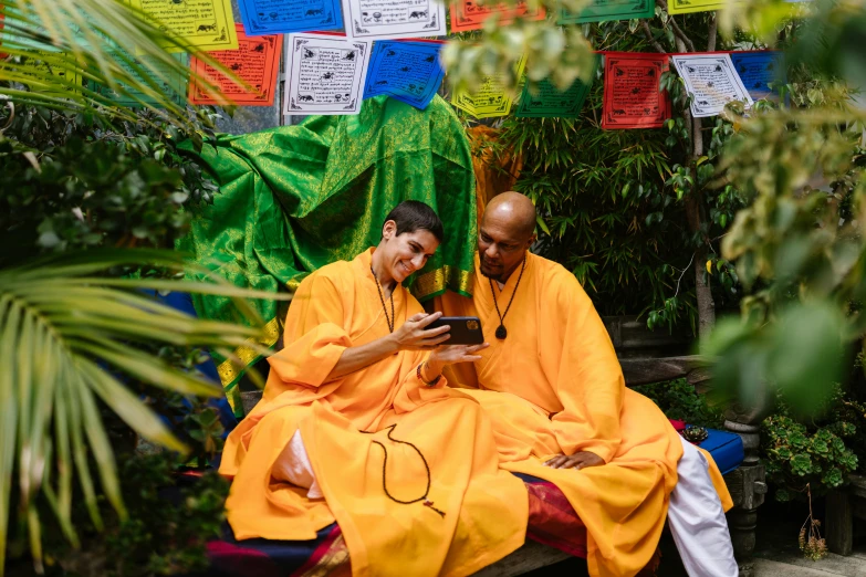 a man with a cell phone sitting next to another man in yellow