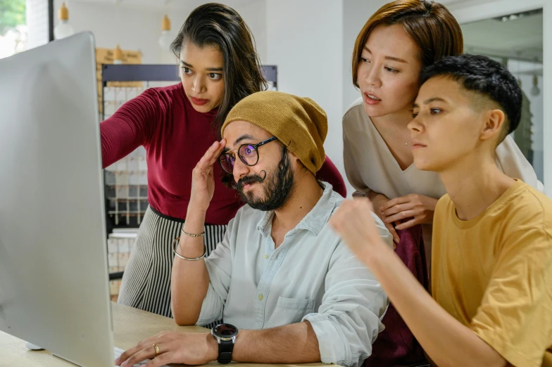 three people looking at a computer screen while one woman puts her hands on the head of another person