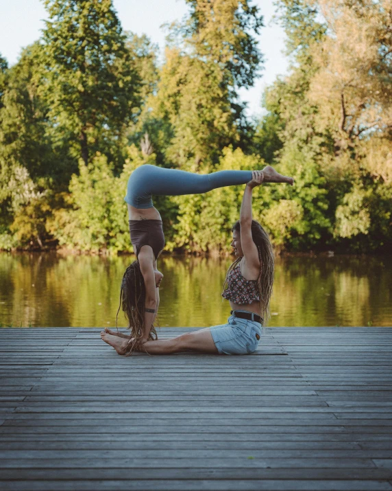 two girls are doing an acrobatic pose on a dock