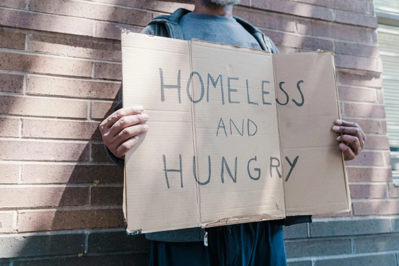 a man in his 40's holding up a cardboard sign that reads homeless and hungry